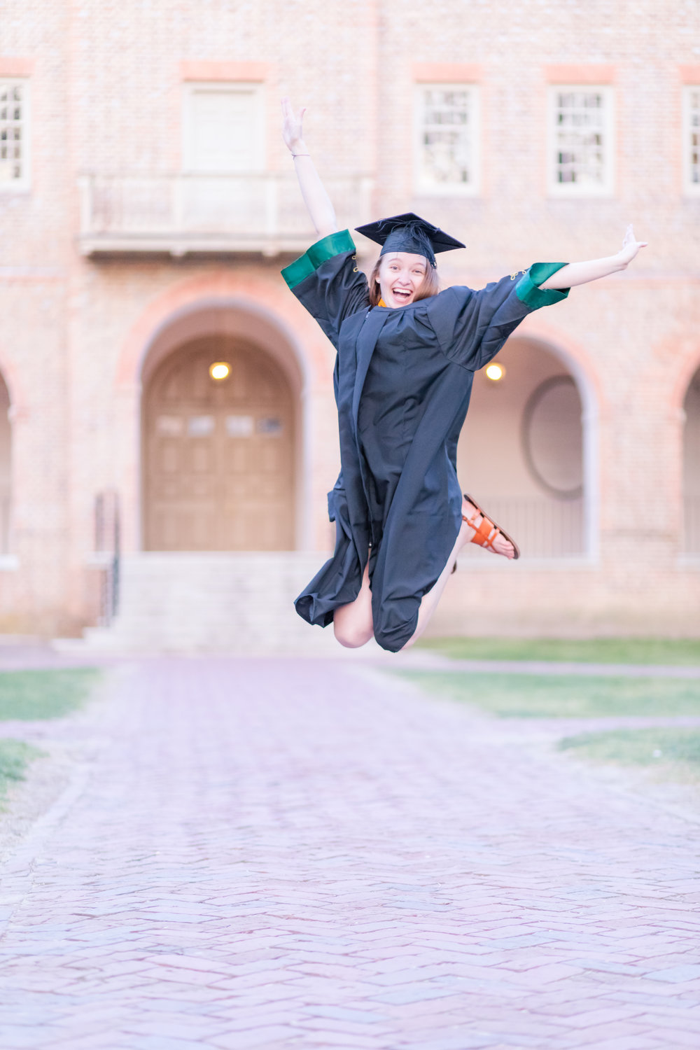 graduate jumping in front of WIlliam and Mary Wren Building for senior portraits