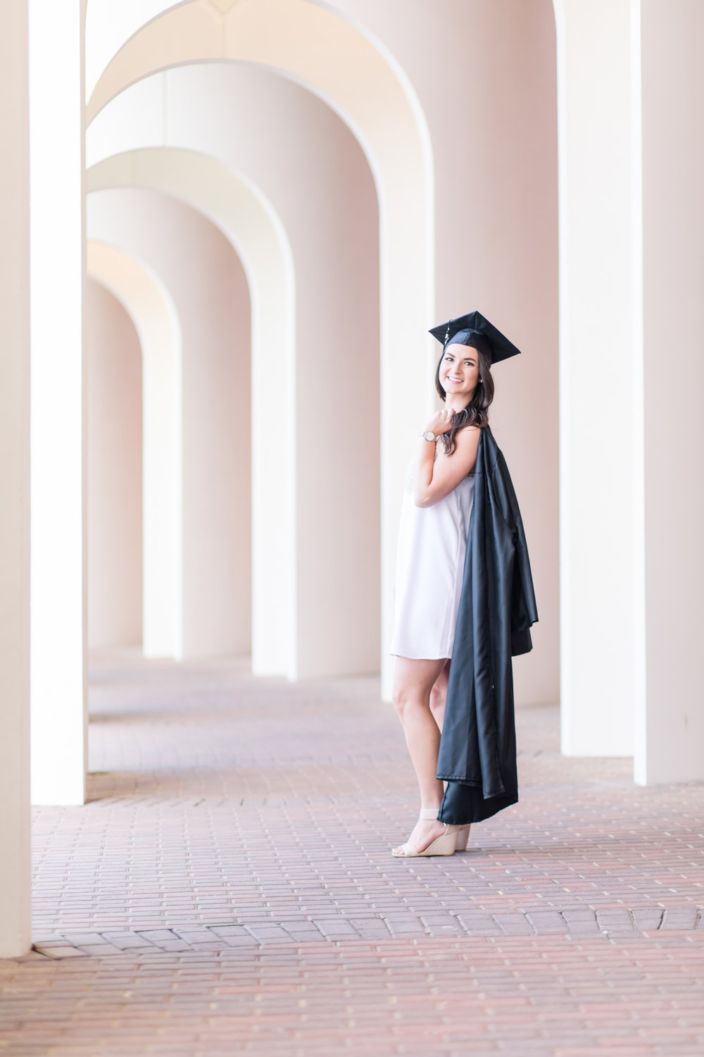 Girl under arches with cap and gown for senior portraits at CNU