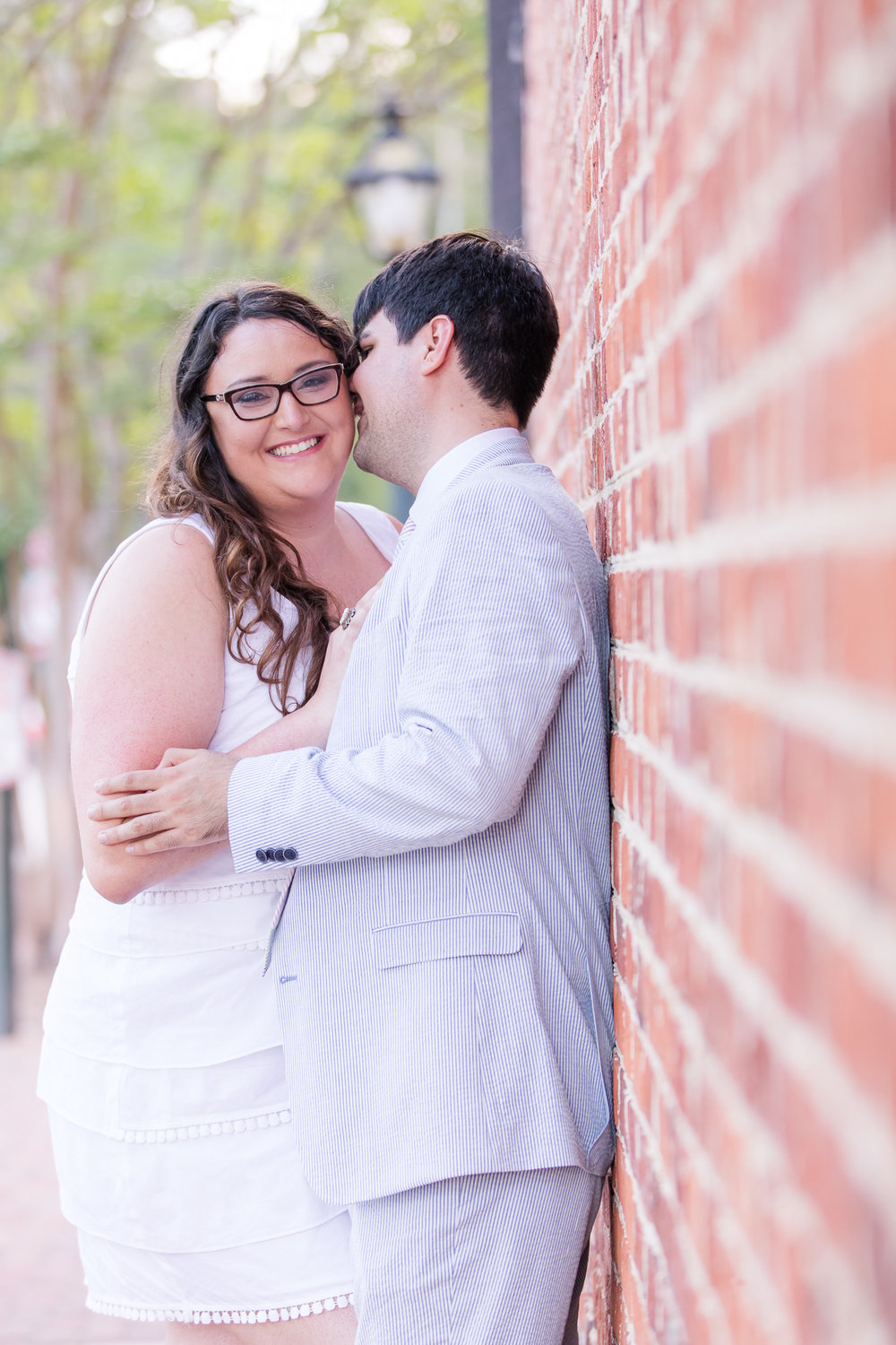 couple leaning on brick wall for surprise engagement photos in Williamsburg, VA