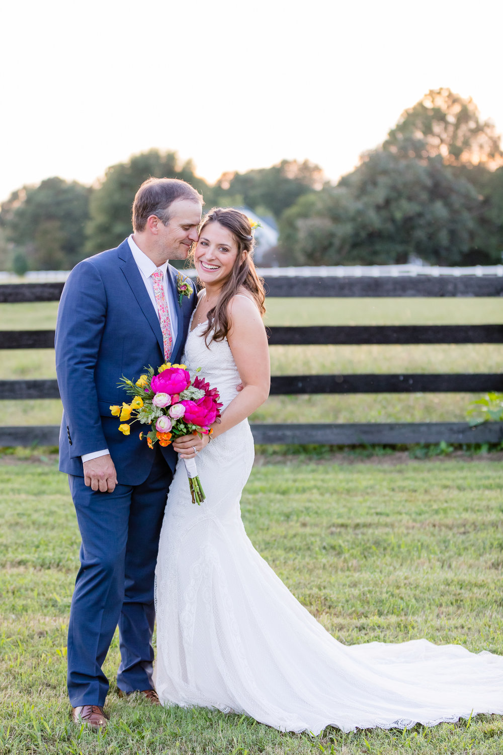 bride smiles at camera while groom nuzzles at golden hour