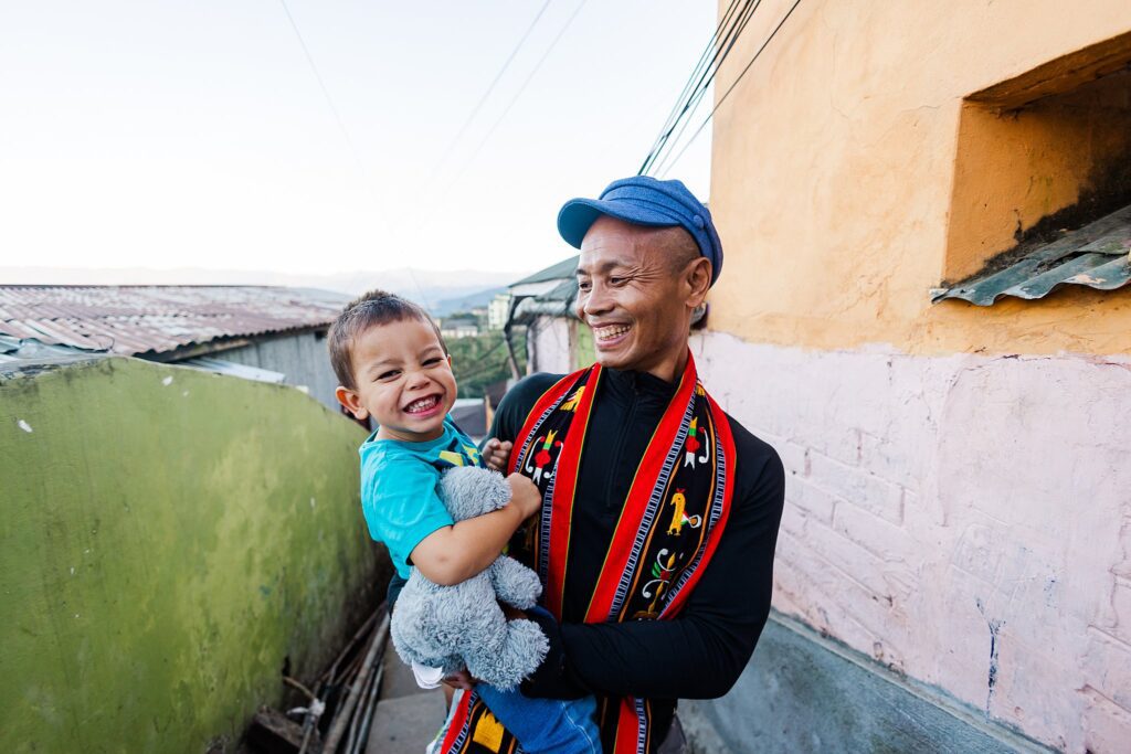 boy cheesy smiles at camera with excitement while dad holds him in Nagaland India travel photography