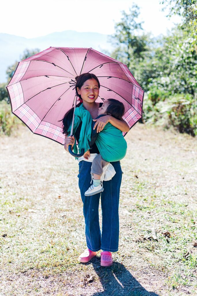 beautiful girl with baby tied to her holds umbrella for shade from son by India travel photographer