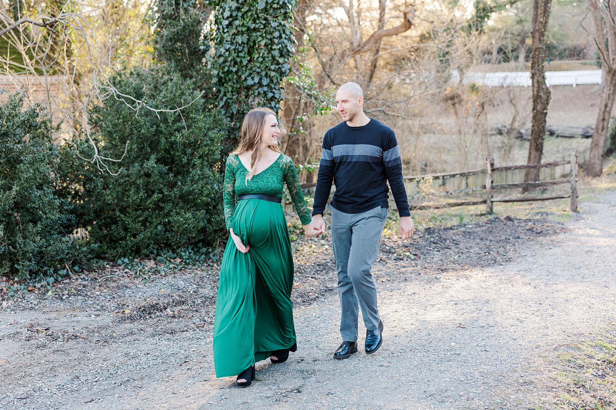 new mom walks in green maternity dress looking back at husband for family photo