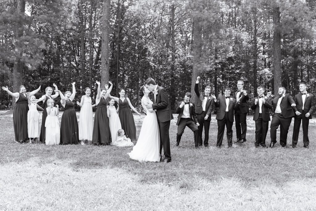 black and white image of wedding party celebrating kiss