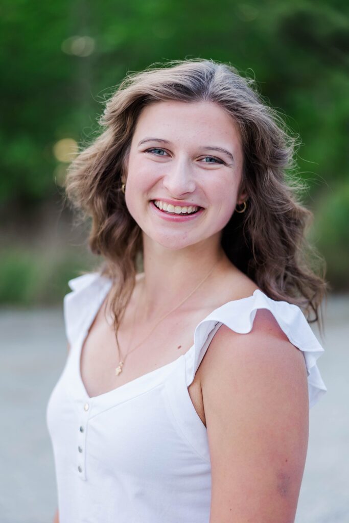 senior smiles for headshot with curly hair and a white tank by senior photographer in Williamsburg, VA
