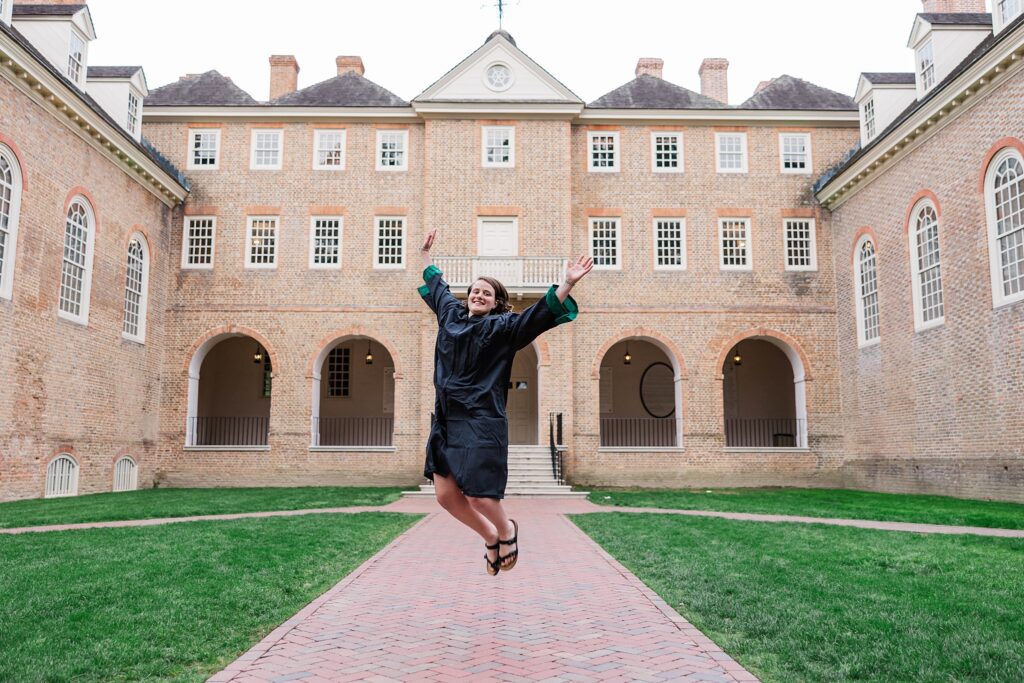senior jumps in cap and gown in front of the Wren Building to celebrate the W&M Class of 2023