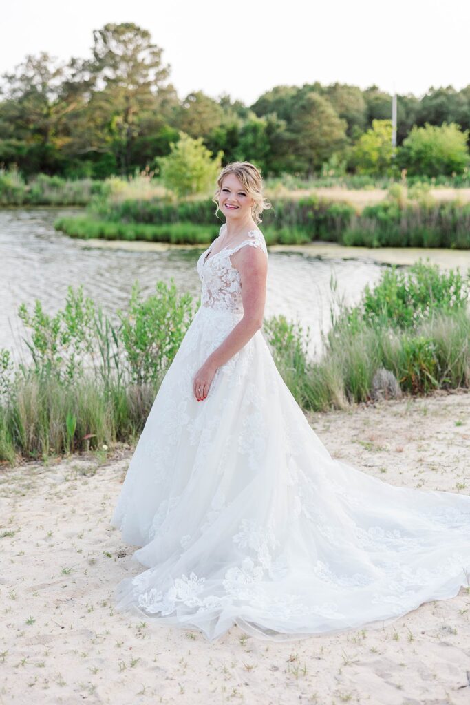 Bride with long train stands in front of water for bridal portraits in Virginia Beach