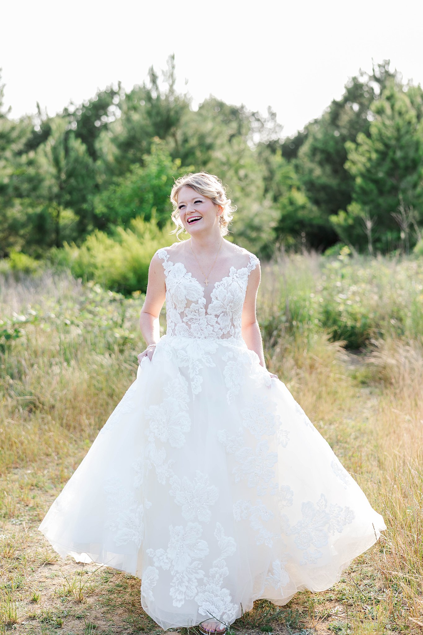 bride stands in full sun in grassy field laughing during bridal portraits in Virginia