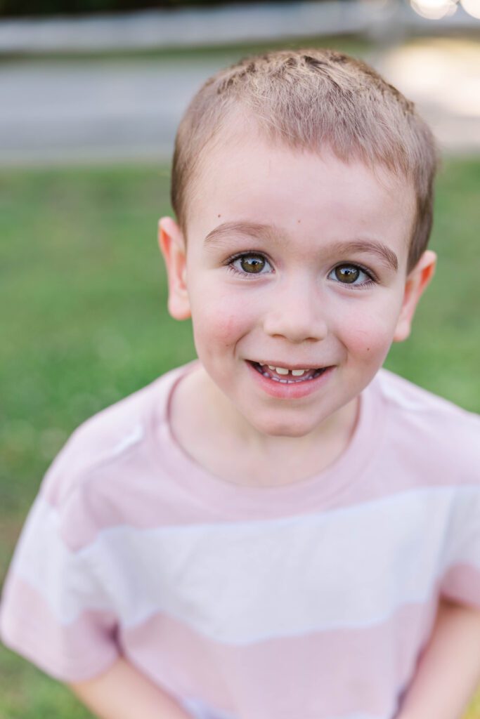 little boy in pink shirt smiles at camera with catchlights in eye