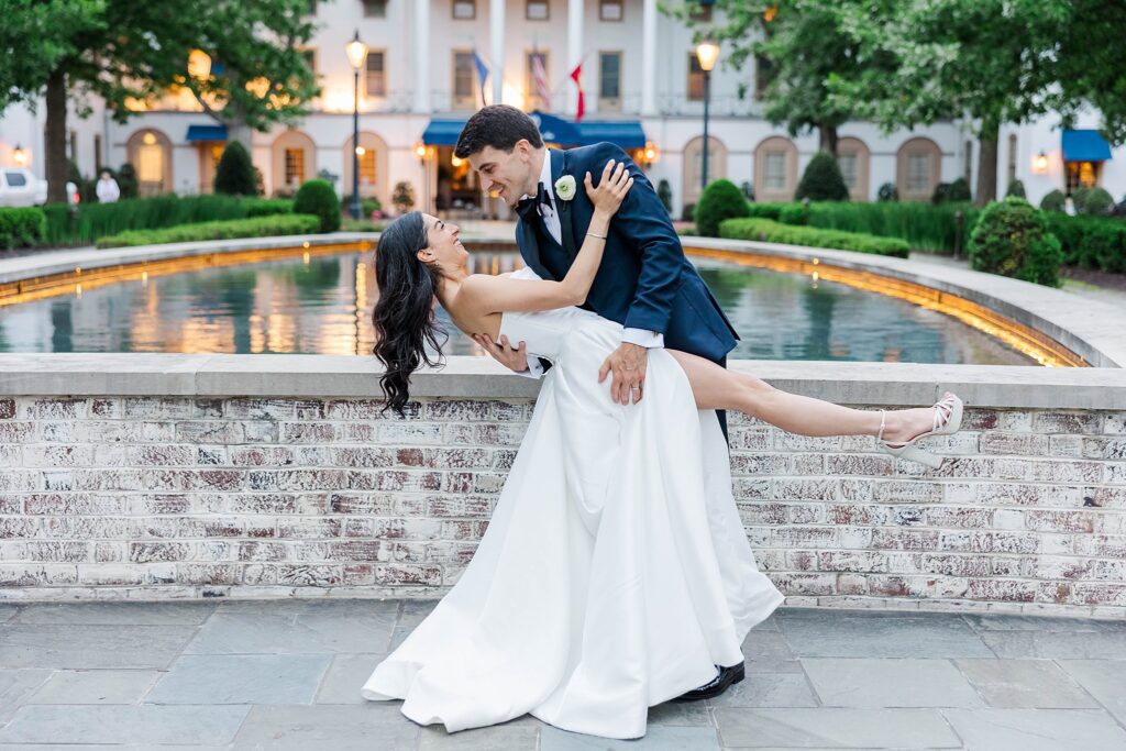 Groom dips bride with slit in dress in front of the Williamsburg Inn fountain after their Wren Chapel Wedding