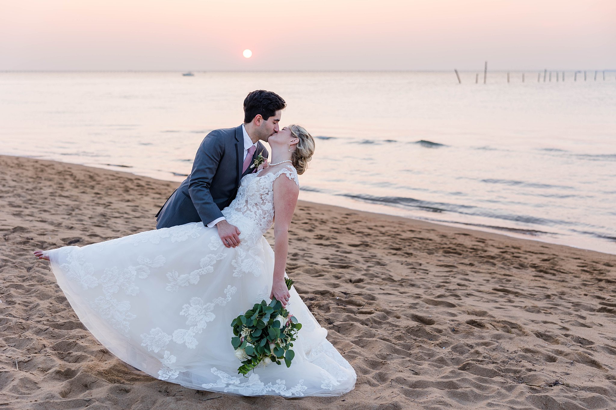 Groom kisses bride while dipping her with sunset behind them at Delta Hotels wedding in VA Beach