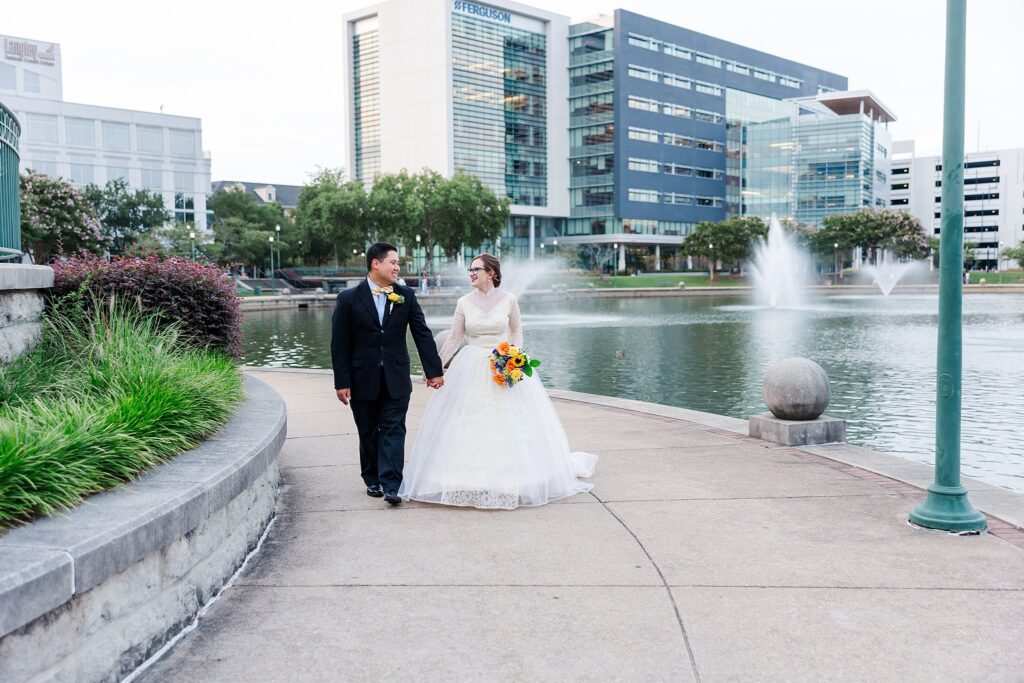 couple walks holding hands in Newport News city center elopement with fountains in background