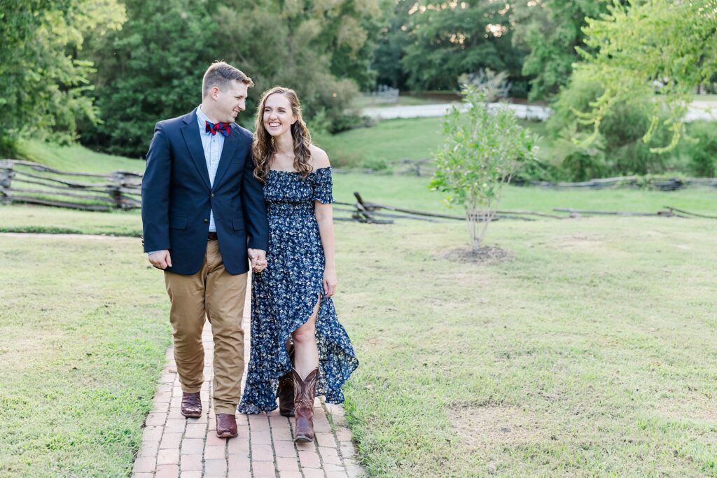 couple walks towards camera with sun glowing behind at Colonial Williamsburg engagement session