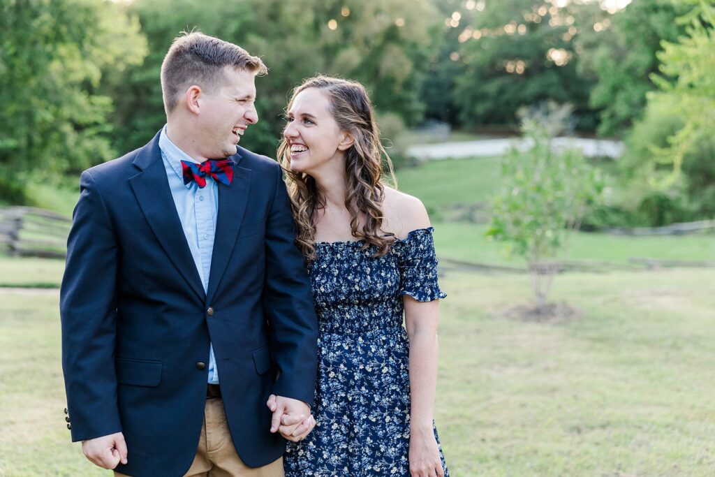 couple laughs while walking with sunlight glowing behind in Colonial Williamsburg engagement session