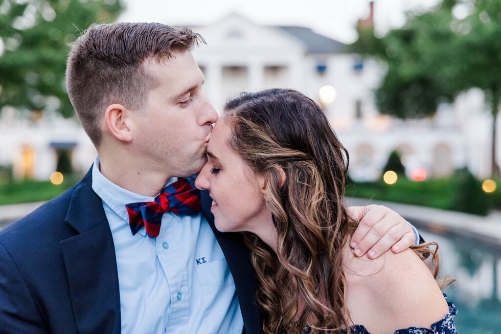 Tyler kisses Emily on forehead in front of the Williamsburg Inn at their fall engagement session