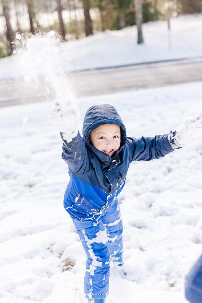 boy throws snow at camera for a fun family photo