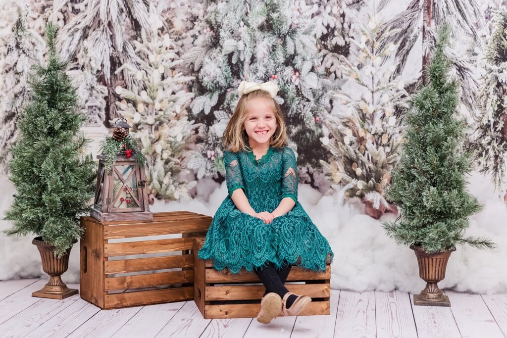 girl smiles with trees and lanterns for Christmas mini sessions in Williamsburg, VA
