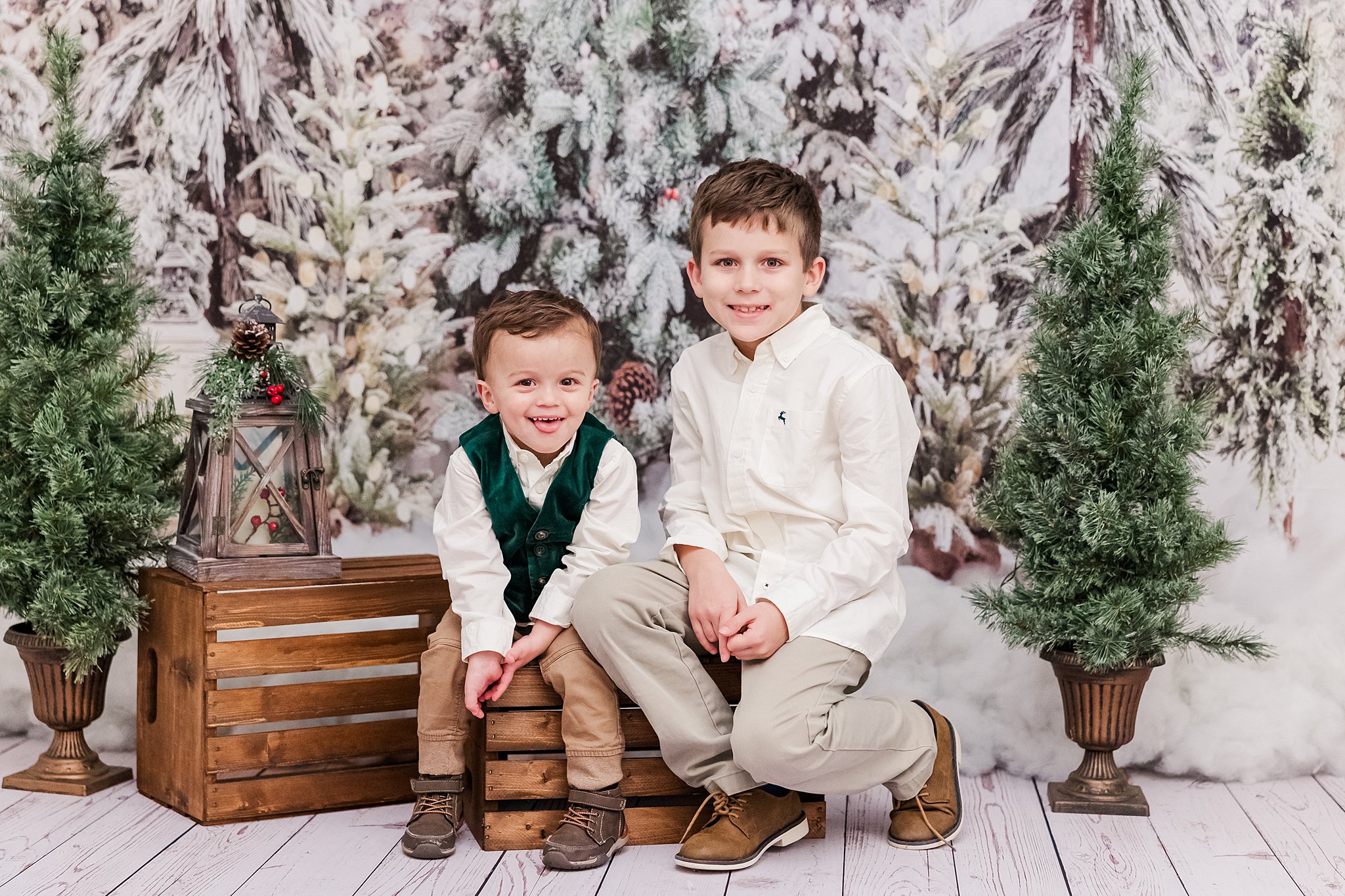 boys smile sitting on wooden crates with snowy backdrop for Christmas mini sessions in Williamsburg, VA