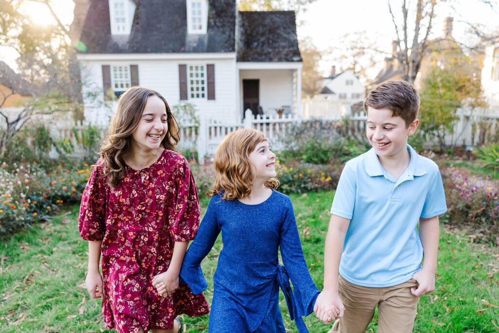siblings walk and smile at each other for family mini sessions in Colonial Williamsburg 