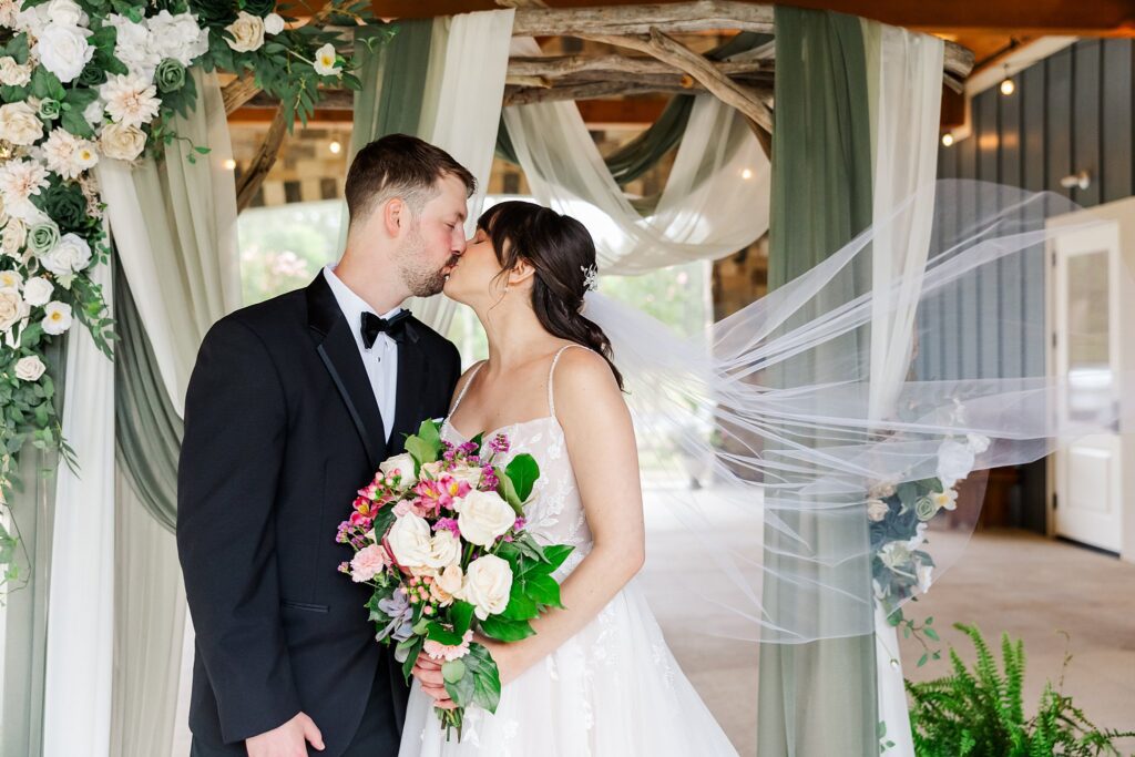bride and groom kiss with veil flowing at their wedding at the Maine of Williamsburg