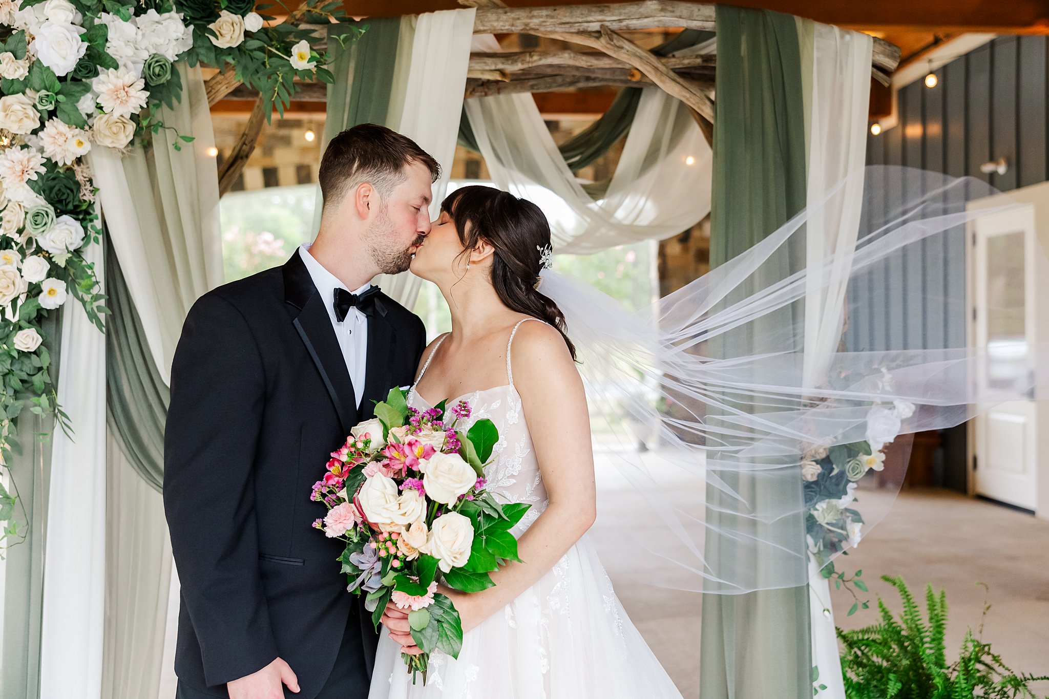 Veil swoops while bride and groom kiss after their wedding at the Maine of Williamsburg