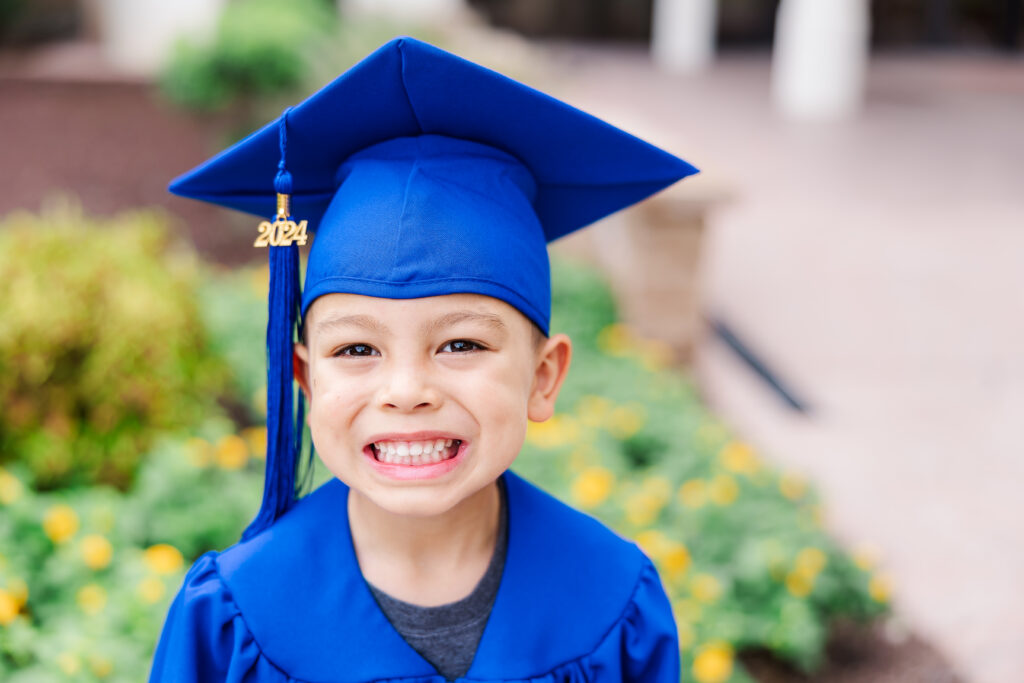 Preschool graduate with blue cap and gown smiling at camera as a part of photographing milestones blog